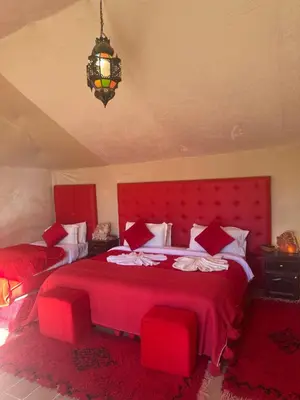 a bedroom with two red beds and a chandelier at Morocco Sahara Desert Camp in Merzouga