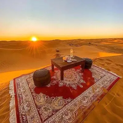 a table in the middle of a desert with the sunset at luxury camp Oasis Opal in Merzouga