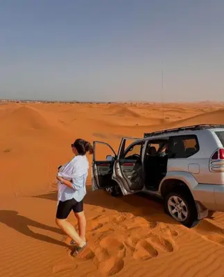 a woman standing in the desert next to a vehicle in the desert at Luxury Stars Camp in Merzouga