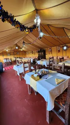 a dining room with tables and chairs in a tent at sahara desert camp in Merzouga