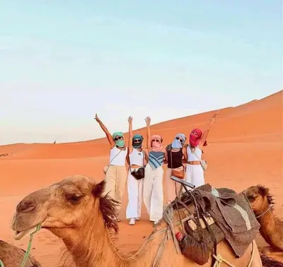 a group of people standing in the desert on a camel at Merzouga Dream Camp in Merzouga