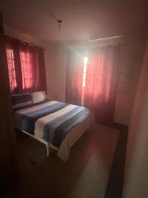 a bedroom with a bed and two windows with red curtains at Étage dans une villa avec piscine partagée Meknès in Meknès