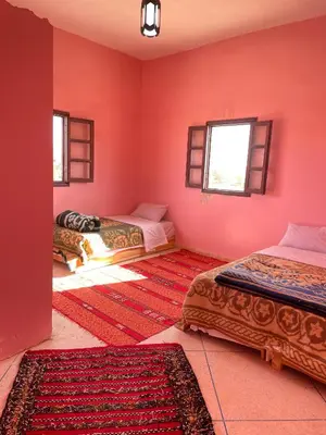 a room with two beds and a red wall at Maison zahra merzouga in Merzouga