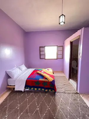a bedroom with purple walls and a bed with a colorful blanket at Maison zahra merzouga in Merzouga