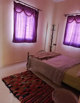 a bedroom with purple curtains and a bed with a rug at taddart in Merzouga