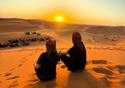 two women sitting in the desert watching the sunset at Merzouga Atlantis in Merzouga