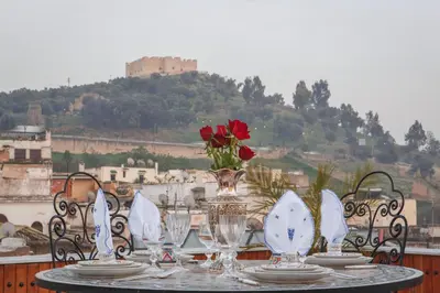 a table with plates and glasses and a vase with roses at Riad Fes Maya suite & spa in Fès