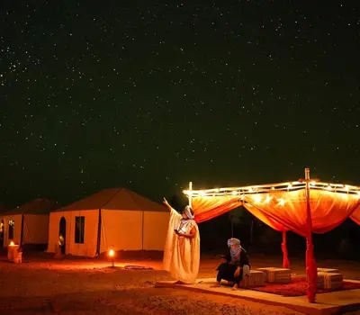 a couple of people sitting under a tent at night at Camping Activities Merzouga in Merzouga