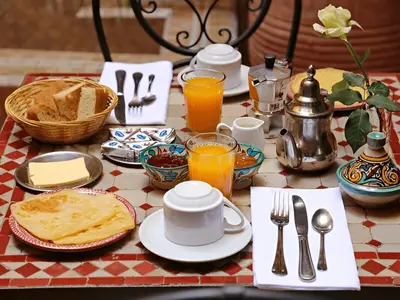 a table topped with plates and utensils and orange juice at Arsura Luxury Camp in Merzouga