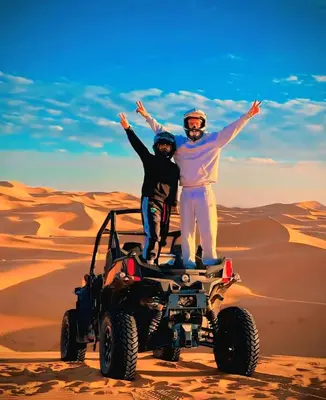 two people standing on top of a wheeler in the desert at Merzouga Standard Camp in Merzouga
