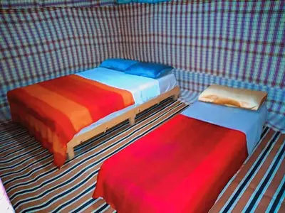 three beds in a room with striped carpet at Merzouga Standard Camp in Merzouga