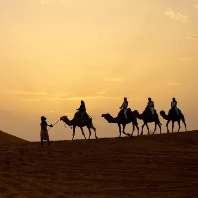 a group of people riding camels in the desert at Royal Erg Chebbi Luxury Camp in Hassilabied