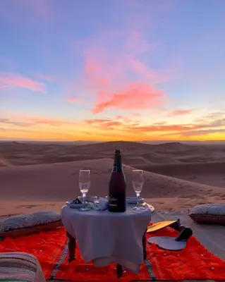 a table with a bottle and two glasses on the desert at Royal Erg Chebbi Luxury Camp in Hassilabied