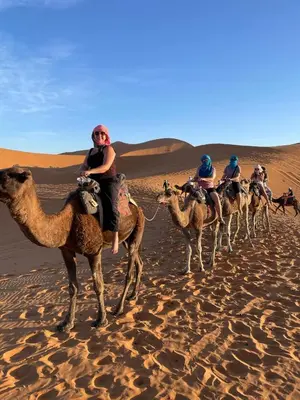 a group of people riding camels in the desert at Aziz luxury camp in Merzouga