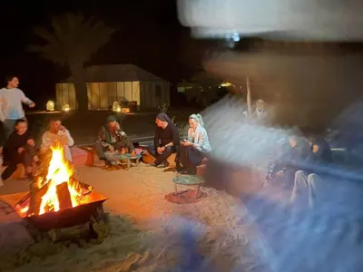 a group of people sitting around a fire in the sand at Aziz luxury camp in Merzouga