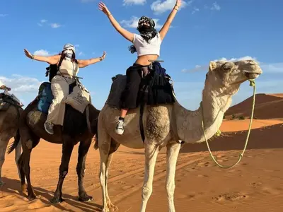 two people riding on a camel in the desert at Global Desert Luxury Camp in Merzouga