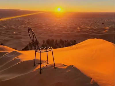 a chair sitting in the desert at sunset at Global Desert Luxury Camp in Merzouga