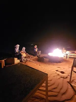 a group of people sitting around a fire at night at Family Dunes Camp in Merzouga