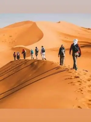 a group of people walking on a sand dune at Family Dunes Camp in Merzouga