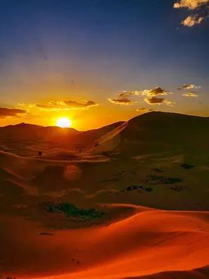 a sunset in the desert with the sun setting at Family Dunes Camp in Merzouga