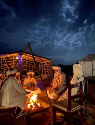 a group of people sitting around a fire at night at Merzouga palace camp in Merzouga