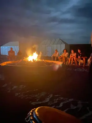 a group of people sitting around a fire on the beach at Desert Family Camp in El Gouera