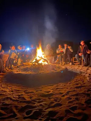 a group of people sitting around a fire on the beach at Desert Family Camp in El Gouera