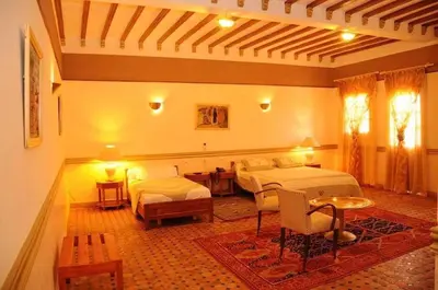 a bedroom with two beds and a table and chairs at Riad Ksar Assalassil Erfoud in Erfoud
