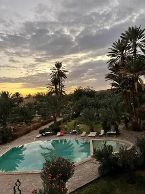 a pool with chairs and palm trees and a sunset at Riad Ksar Assalassil Erfoud in Erfoud
