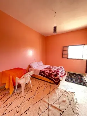 a bedroom with orange walls and a bed and a chair at Sahara desert Maison in Merzouga
