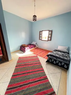 two beds in a room with a rug at Sahara desert Maison in Merzouga