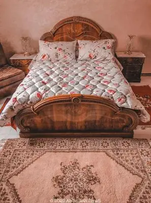 a bed with a wooden headboard and a rug at casa medina sanaa in Oulad Akkou