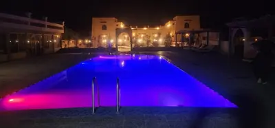 a swimming pool at night with purple lights at riad tighmart in Merzouga