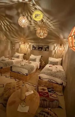 a bedroom with two beds and a table and chandeliers at Haven Luxury Camp in Merzouga