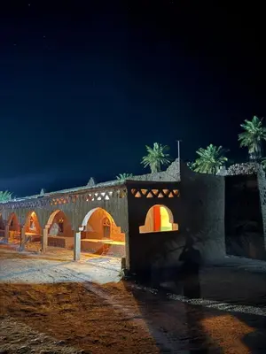 a building with an archway and palm trees at night at Auberge el oasis mharech in Foum Mharech