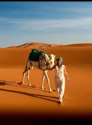 a woman walking in the desert with a camel at Merzouga desert camp in Merzouga