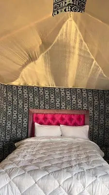 a bedroom with a white bed with a red headboard at Desert Moon Camp in Merzouga