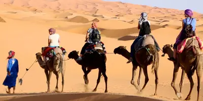 three people riding on camels in the desert at Desert Moon Camp in Merzouga