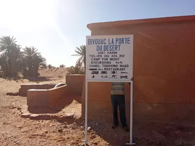 a person standing next to a sign in the desert at Bivouac Porte du Désert in Mhamid