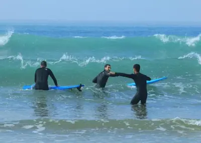 a group of three men in the ocean with surfboards at Baie D'AGADIR in Oulad Akkou