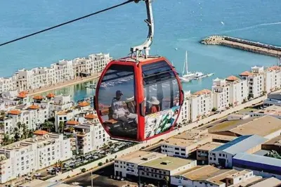 a red cable car flying over a city at Baie D'AGADIR in Oulad Akkou