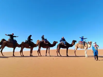 a group of people on camels in the desert at Merzouga Unique Standard Camp in Merzouga