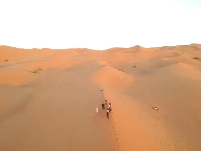 a group of people walking through the desert at Merzouga Unique Standard Camp in Merzouga