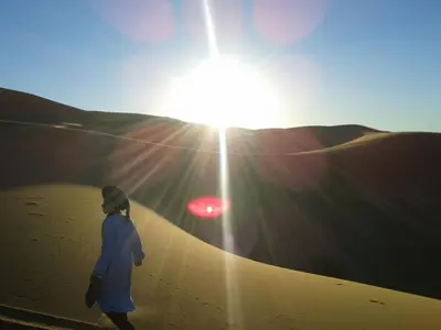 a person walking in the desert with the sun shining at Chams Luxury Camp in Lac Yasmins
