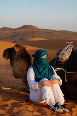 a person sitting next to a camel in the desert at Moonrise Luxury Camp in Merzouga