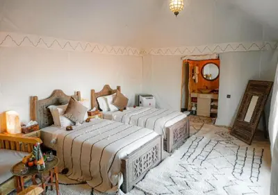 a bedroom with two beds and a table and a mirror at Dunes Light Luxury camp in Merzouga