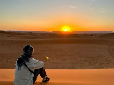 a woman sitting in the desert watching the sunset at Erg Palace Luxury Camp in Merzouga