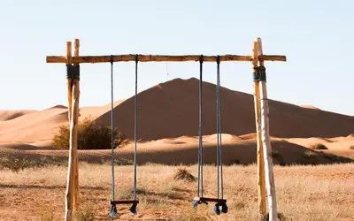an old swing in the desert with a mountain in the background at Desert Paradise Lodging in Merzouga