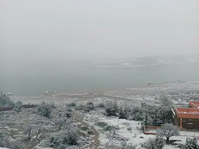 a snow covered field with a house and a lake at Tigmi Nlkhir in Aït Irizane