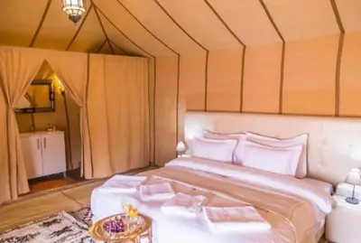 a bedroom with a large white bed with a table at Merzouga Luxury Camp & Desert Activities in Merzouga
